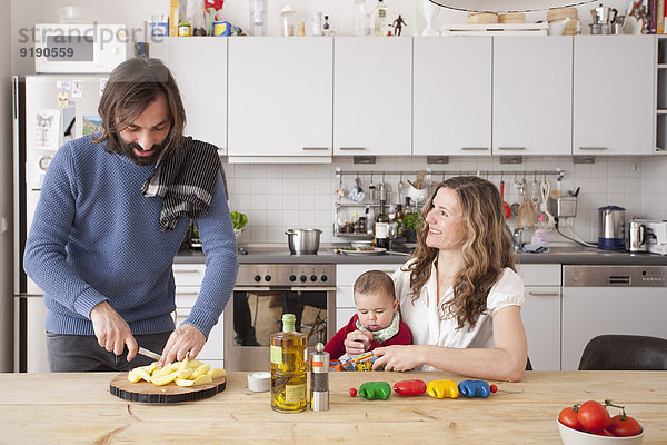Vater hackt Gemüse mit Frau und Mädchen in der Küche