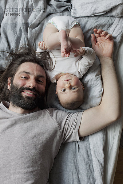 Porträt des lächelnden Vaters und des Mädchens im Bett liegend