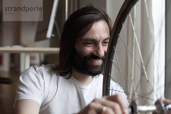 Lächelnder erwachsener Mann  der das Fahrrad zu Hause repariert.