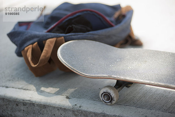 Nahaufnahme von Skateboard und Tasche auf dem Bürgersteig