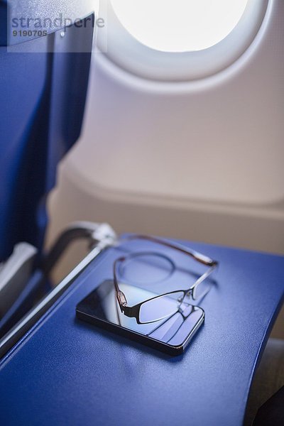 Smartphone und Brille auf dem Tisch im Flugzeug