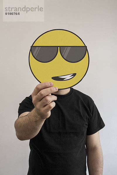 Mann hält eine coole Sonnenbrille mit Emoticon-Gesicht vor seinem Gesicht.