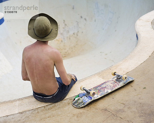 Rückansicht eines Mannes mit Skateboard am Rand einer Skateboard-Schüssel