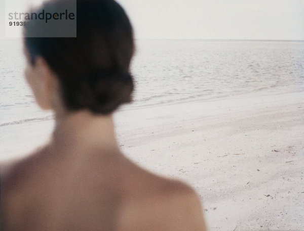 Frau mit Blick auf den Ozean  Rückansicht von Kopf und Schultern  Strandfokus im Hintergrund