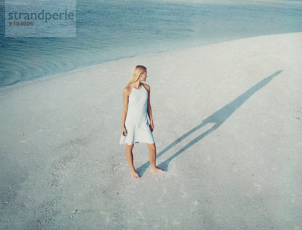Frau  die am Strand steht und ihren Schatten betrachtet.