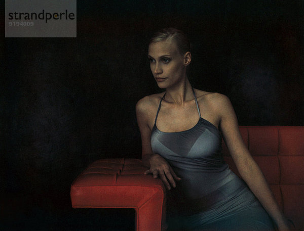 Elegante junge Frau auf dem Sofa sitzend  auf dem Ellenbogen lehnend  wegschauend