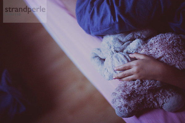 Kind auf dem Bett liegend  Plüschtiere haltend  abgeschnitten