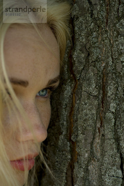 Junge Frau lehnt sich an den Baumstamm und schaut traurig weg.