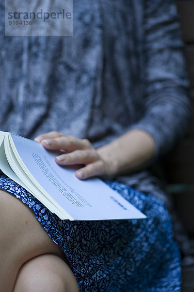 Frau sitzend mit geöffnetem Buch auf dem Schoß  beschnitten