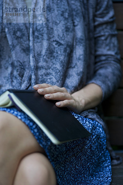 Frau sitzend mit geöffnetem Buch auf dem Schoß  beschnitten