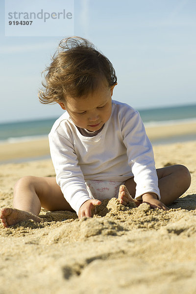 Kleines Mädchen spielt im Sand am Strand