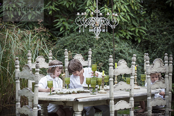 Kinder sitzen am kunstvollen Esstisch im Freien