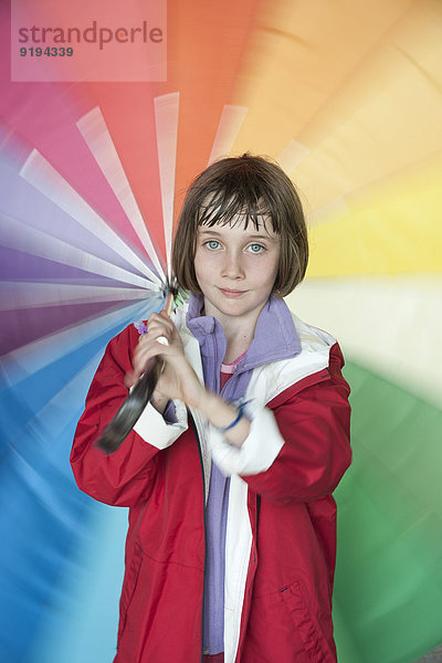 Mädchen spinnt regenbogenfarbigen Regenschirm