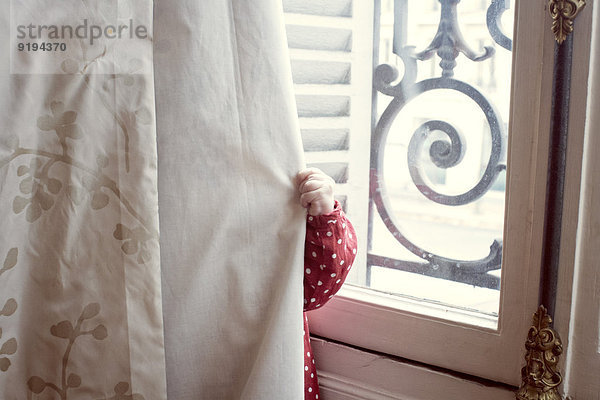 Kind versteckt sich hinter dem Vorhang