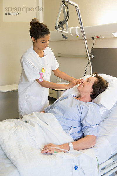 Krankenschwester  die die Patientin auf dem Krankenhausbett behandelt