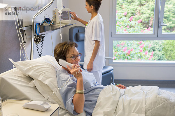 Patientin spricht am Telefon im Krankenhausbett