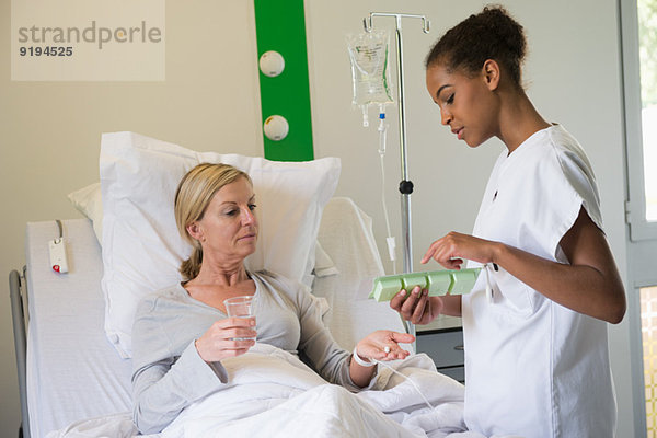 Krankenschwester bespricht Pillenschachtel mit Patientin im Krankenhausbett