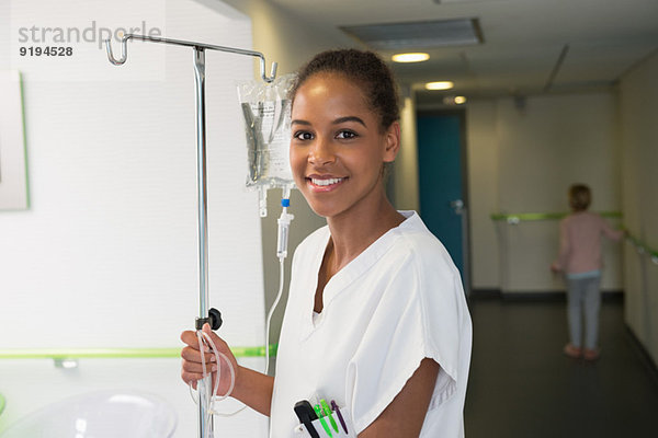 Porträt einer Krankenschwester mit Infusionsständer und Lächeln im Krankenhaus
