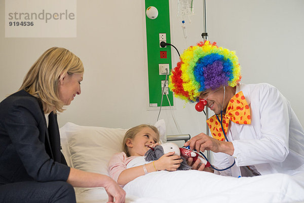 Männlicher Arzt im Clown-Kostüm bringt Patientin zum Lächeln im Krankenhausbett