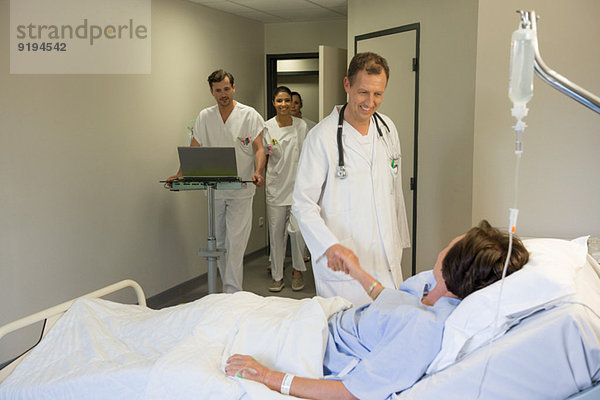 Männlicher Arzt schüttelt dem Patienten die Hand auf dem Krankenhausbett
