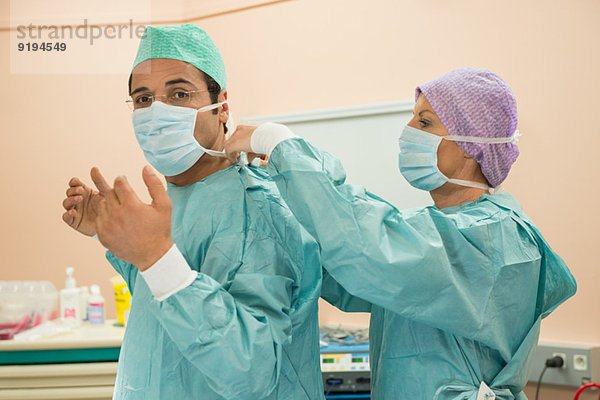 Chirurgin hilft einem Chirurgen beim Anziehen der Schutzkleidung