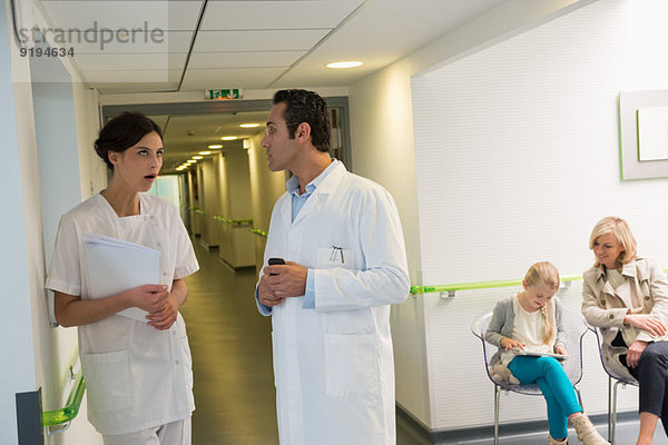 Arzt und Krankenschwester besprechen im Krankenhausflur mit Patienten im Wartezimmer