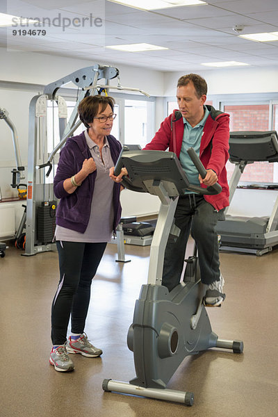 Trainerin hilft einer Frau beim Radfahren im Fitnessstudio