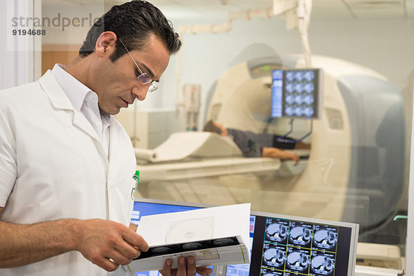 Männlicher Arzt untersucht MRT-Scan-Bericht im medizinischen Untersuchungsraum