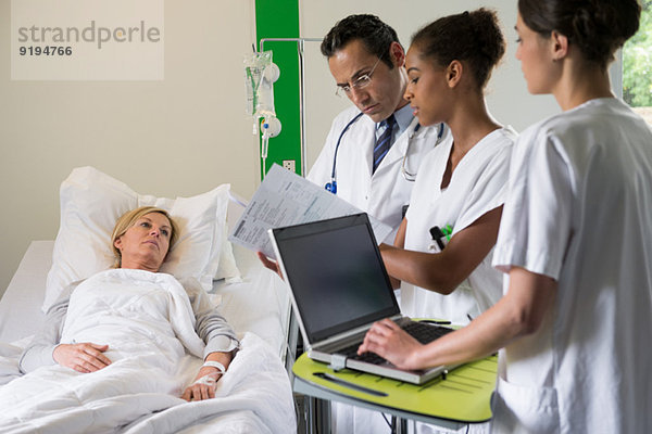 Medizinisches Team bespricht Patientinnenakte im Krankenhausbett