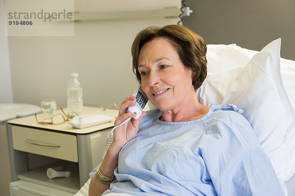 Frau spricht am Telefon im Krankenhausbett