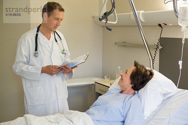 Männlicher Arzt im Gespräch mit dem Patienten auf dem Krankenhausbett