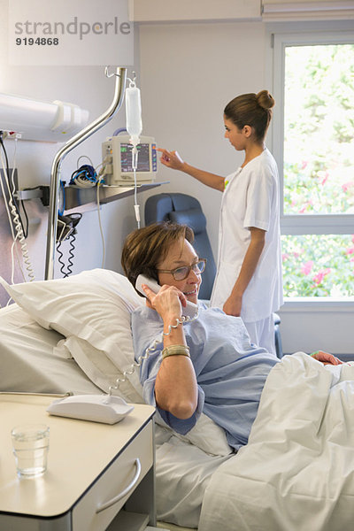 Patientin spricht am Telefon im Krankenhausbett