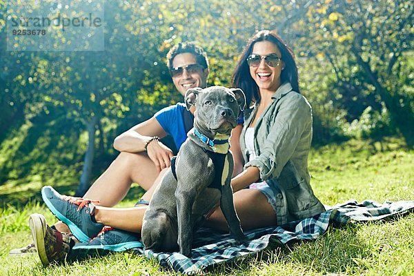 Porträt eines Paares und eines Hundes auf Picknickdecke im Park