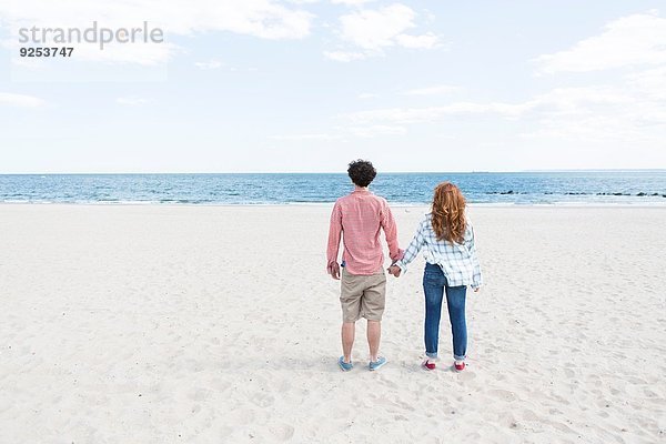 Rückansicht des Paares  das am Strand Händchen hält.