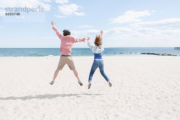 Rückansicht des springenden Paares am Strand