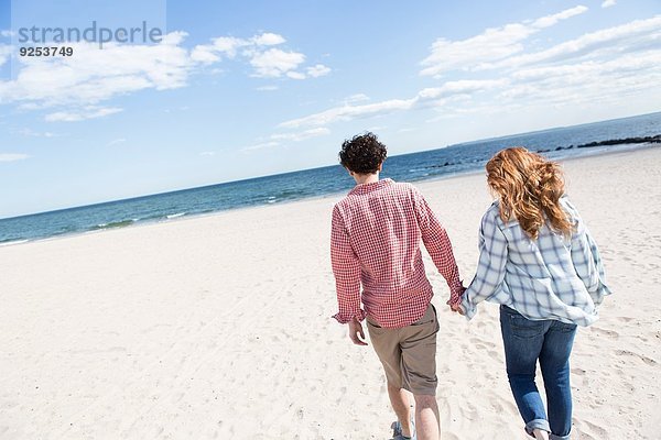 Romantisches Paar  das Hand in Hand am Strand schlendert