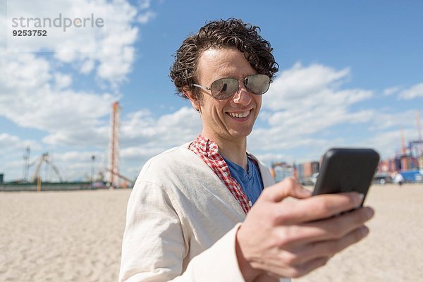 Mid Erwachsene Mann SMS auf Smartphone am Strand