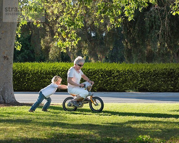 Dreijähriger Junge schiebt Großmutter auf Fahrrad im Park