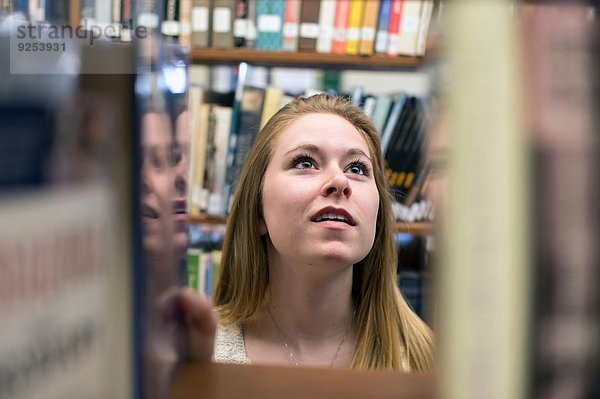 Junge Frau  die ein Buch in der Bibliothek auswählt