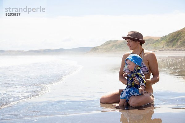 Junge Frau am Strand sitzend mit Baby-Sohn
