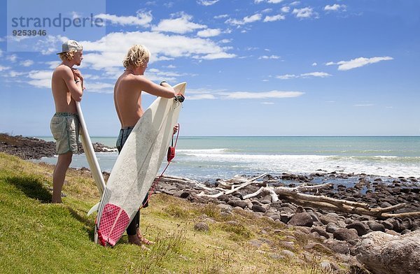 Zwei junge männliche Surferfreunde beobachten das Meer