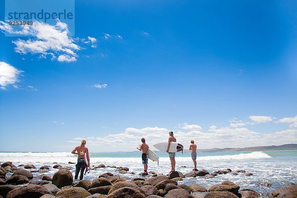 Vier junge männliche Surferfreunde beobachten das Meer