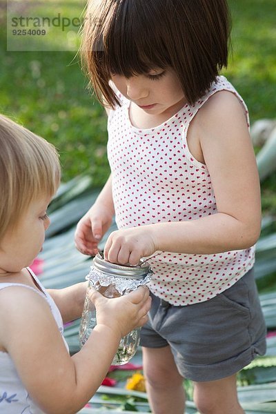 Mädchen und Kleinkind Schwester halten Glas mit grüner Eidechse im Garten