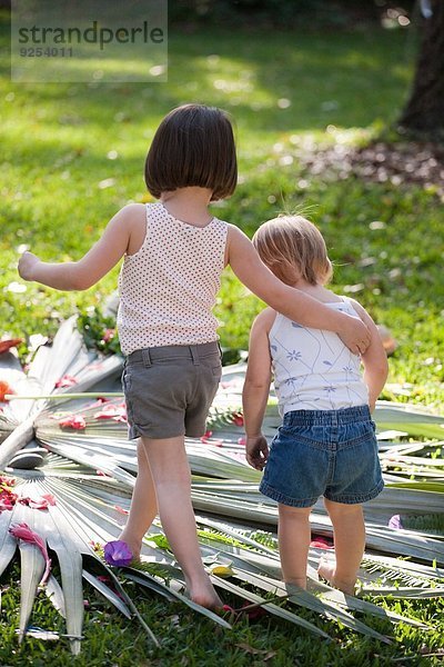 Mädchen mit Arm um Kleinkind Schwester mit Blumen- und Blattdisplay im Garten
