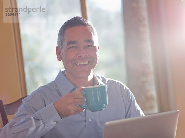 Porträt eines lächelnden reifen Mannes mit Kaffee und Laptop