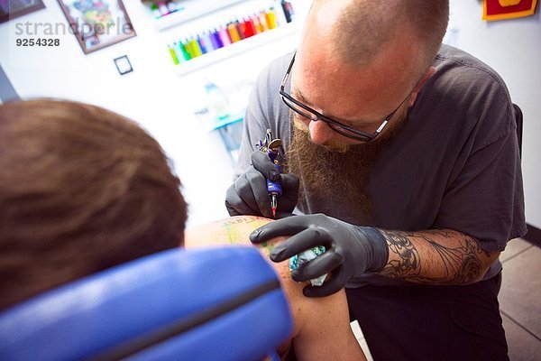 Mittlerer Erwachsener Mann mit tätowierter Schulter im Tattoo-Salon