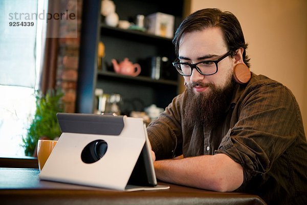 Junger Mann trinkt Kaffee und benutzt digitale Tabletten im Cafe