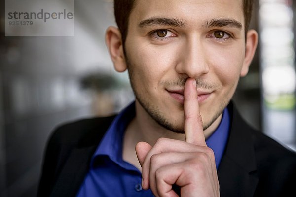 Porträt eines jungen Geschäftsmannes mit Finger auf den Lippen im Büro