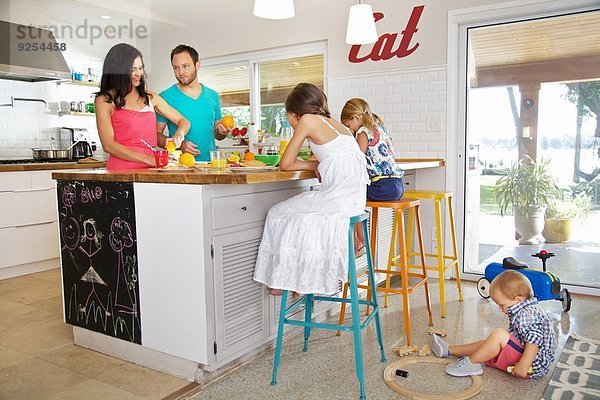 Mittlere erwachsene Eltern und drei Kinder bereiten das Frühstück in der Küche zu.