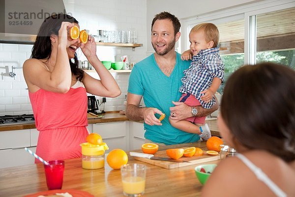 Mutter macht ein Gesicht mit Orangen für ihre Familie an der Frühstückstheke